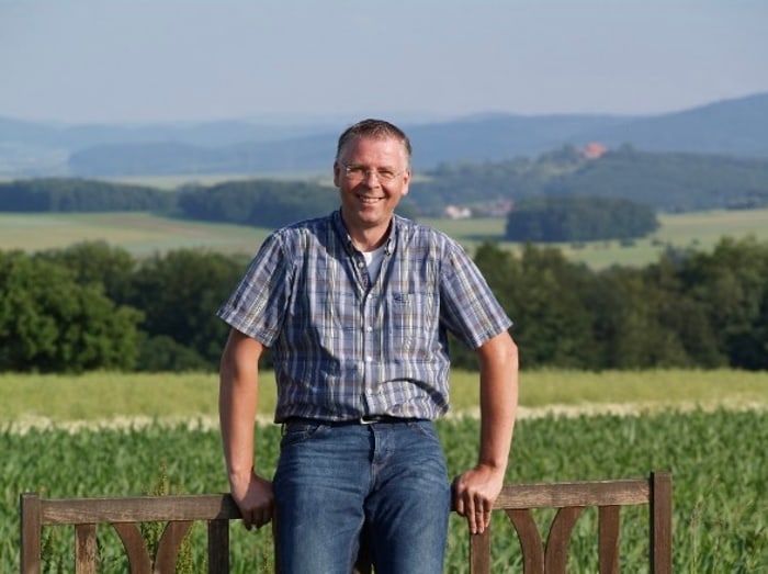 Systemo Gründer Stefan Putz steht auf einer Bank vor einem Feld.